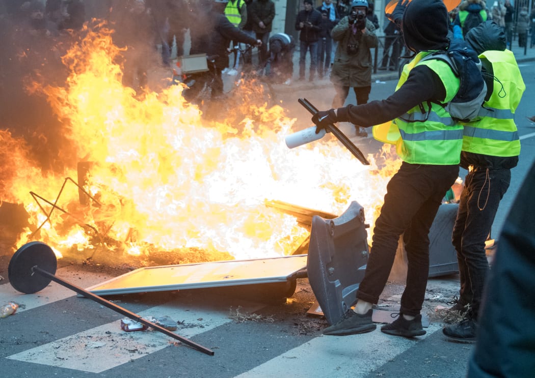 Two Gilet Jaune near a barricade on fire near the Gare Saint-Lazare on December 8, 2018 in Paris, France.