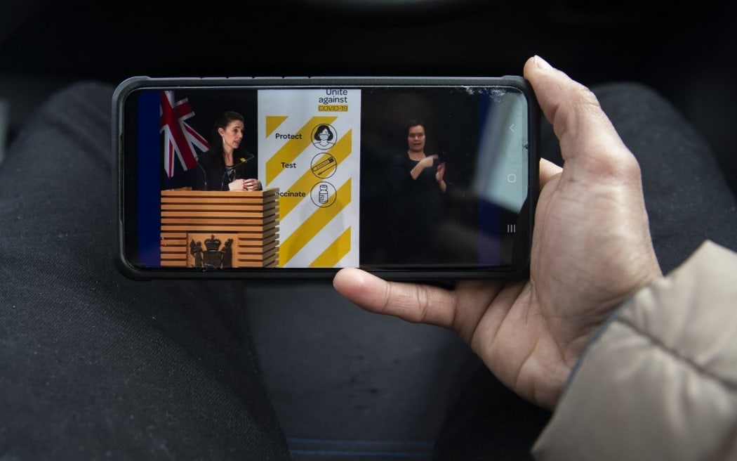 A man watches a live press conference of New Zealand Prime Minister Jacinda Ardern (L) in Christchurch, New Zealand, on August 27, 2021. Ardern has confirmed Auckland will remain in alert Level 4 lockdown until 31st August 2021 as the country battles with the latest COVID-19 outbreak.