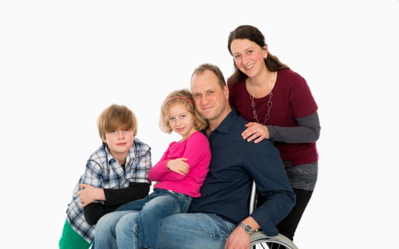 A photo of a disabled man in wheelchair with his family in front of white background