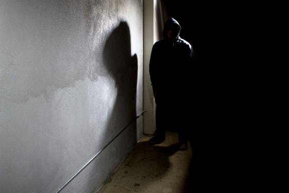 hooded criminal stalking in the shadows of a dark street alley alleyway