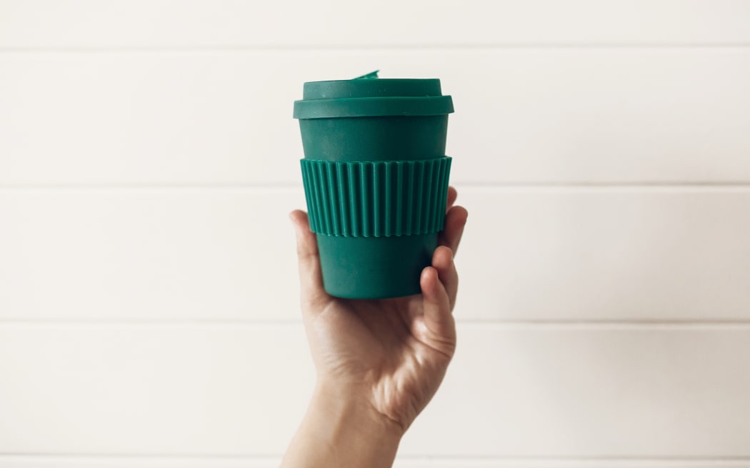 Concept zéro déchet.  Main tenant une élégante tasse à café écologique réutilisable sur un fond en bois blanc.  Tasse verte en fibre de bambou naturel.  Interdire le plastique à usage unique.  choisir.