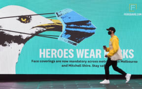 A man walks past a sign urging people to wear face masks in Melbourne on August 14, 2020 as the city battles an outbreak of the COVID-19 coronavirus.