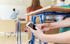 A student texting in a classroom under his desk during a lesson.