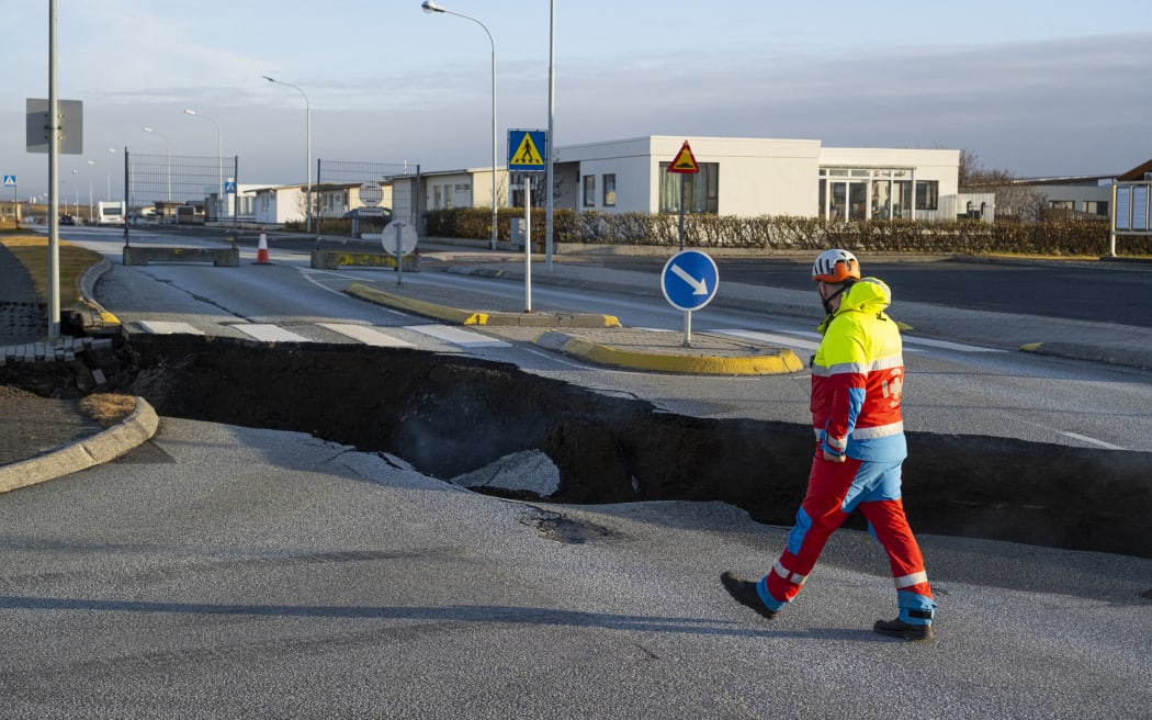 Esta foto, tomada el 13 de noviembre de 2023, muestra a un miembro de los servicios de emergencia caminando cerca de una grieta en la carretera principal de Grindavik, en el suroeste de Islandia, tras los terremotos.  La ciudad, donde viven unas 4.000 personas, fue evacuada en las primeras horas del 11 de noviembre, después de que el movimiento de magma bajo la corteza terrestre provocara cientos de terremotos, que los expertos advirtieron que podrían ser un precursor de una erupción volcánica.