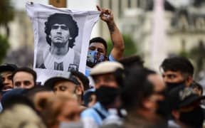 A man waves t-shirt with a picture of Diego Maradona as fans wait to enter Government House to pay tribute to the late football legend, Buenos Aires, 26 November.