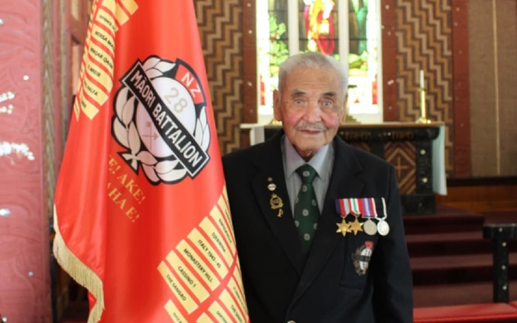 Tā Robert Gillies Kamupene B, 28 (Māori) Battalion stands with Aake Ake Kia Kaha, The 28 (Māori) Battalion  Battle Honours Memorial Flag at St Faiths, Ohinemutu.