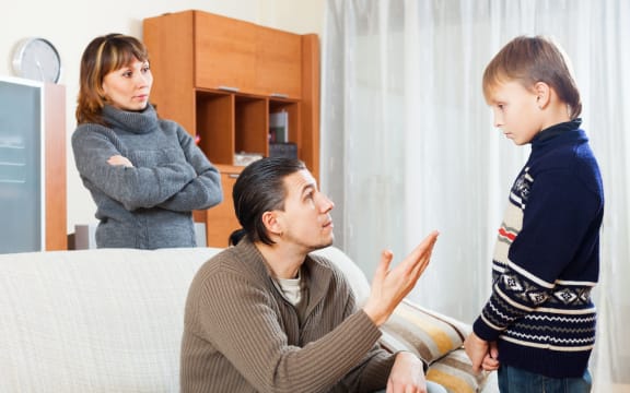 A photo of serious parents berating their teenage son at home