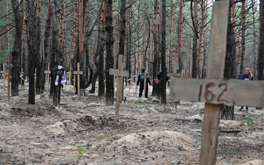 Policías ucranianos caminan entre cruces en un bosque en las afueras del este de Ucrania el 16 de septiembre de 2022.  Después de recuperar la ciudad oriental de las fuerzas rusas, Ucrania dijo que contó 450 tumbas en una sola fosa común cerca de Isium.