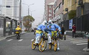 Health workers in personal protective equipment (PPE) carrying Covid-19 coronavirus testing swabs and tubes are seen on bicycles on a Beijing street, 24 November, 2022.