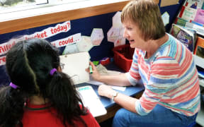 A teacher's aide sit beside a pupil she is helping with writing