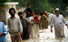 Displaced people wade through a flooded area in Peshawar, Khyber Pakhtunkhwa, Pakistan on August 27, 2022. Since June, nearly 900 people have died by severe monsoon rains and floods in Pakistan, while thousands have been displaced and millions more affected. Thousands of people who live in areas under threat of flooding have been told to evacuate.