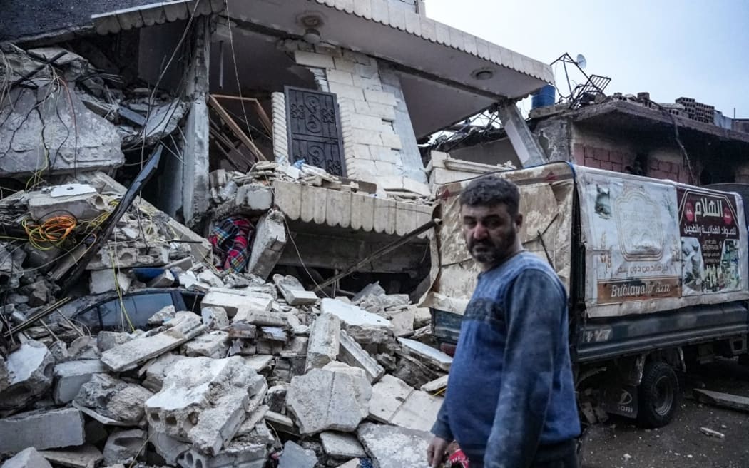 A resident stands in front of  a collapsed building following an earthquake in the town of Jandaris, in the countryside of Syria's northwestern city of Afrin in the rebel-held part of Aleppo province, on February 6, 2023. - Hundreds have been reportedly killed in north Syria after a 7.8-magnitude earthquake that originated in Turkey and was felt across neighbouring countries. (Photo by Rami al SAYED / AFP)