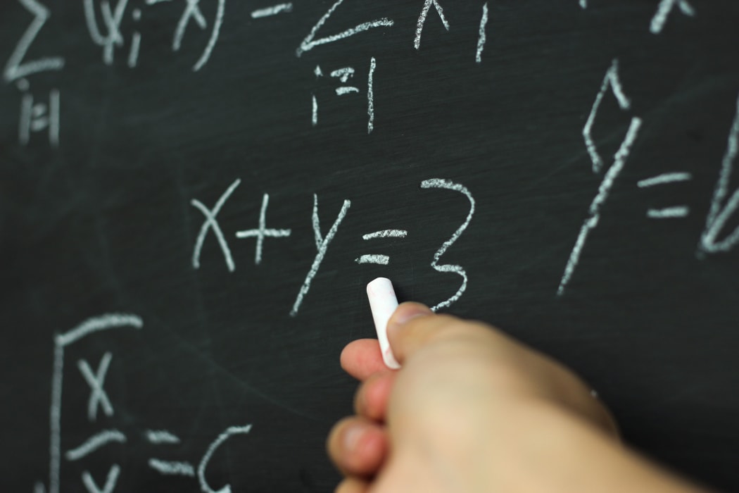 A teacher uses a blackboard to solve a mathematics equation.