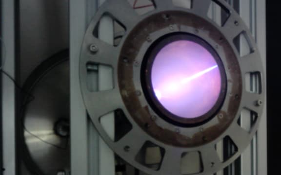A large metal cylinder embedded in beams with a glowing purple light emanating from its centre.
