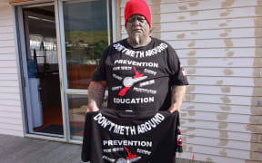 Heavily tattooed man in anti "p" t-shirt stands on his deck