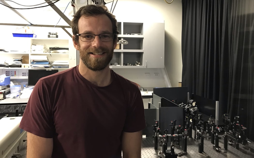 Dr Michael Price is smiling and standing in front of a laser set up.
