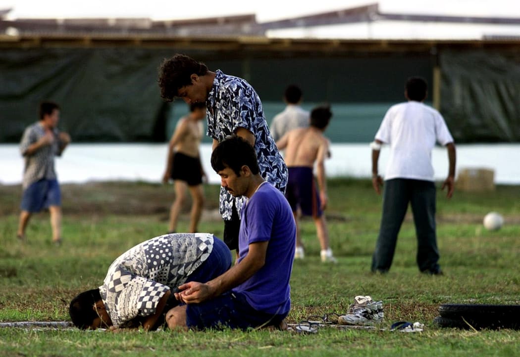 A small group of Muslim refugees pray at sunset while other refugees (background) participate in a football match at a camp for the asylum seekers on the small island of Nauru, 20 September 2001.