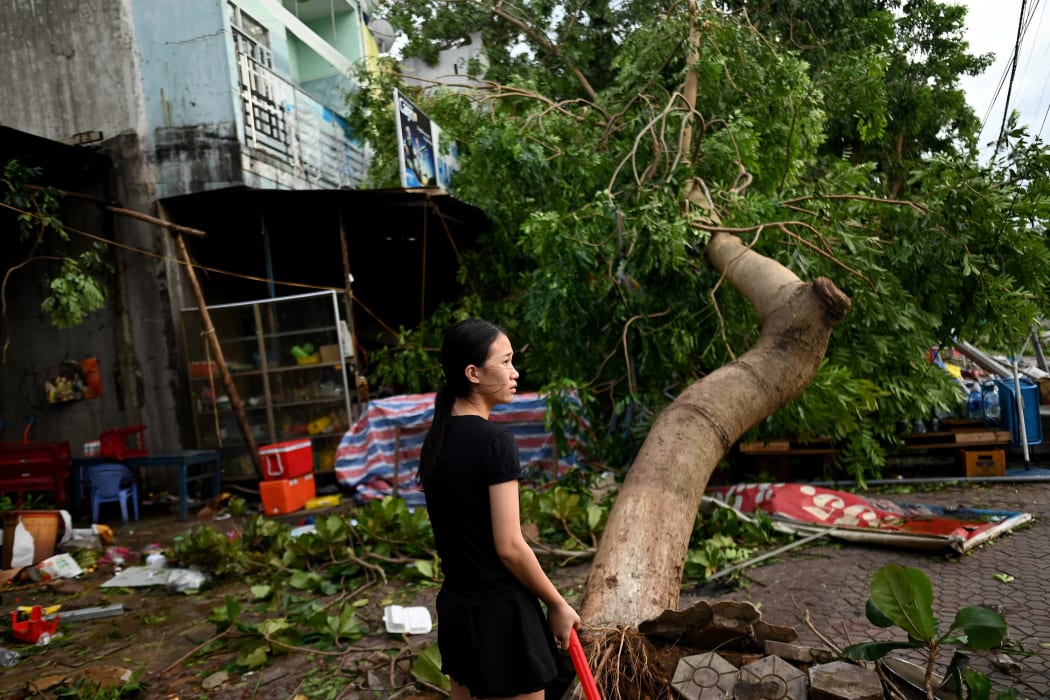 A woman clears debris outside an eatery next to uprooted trees in central Vietnam's Quang Ngai province in the aftermath of Typhoon Molave.