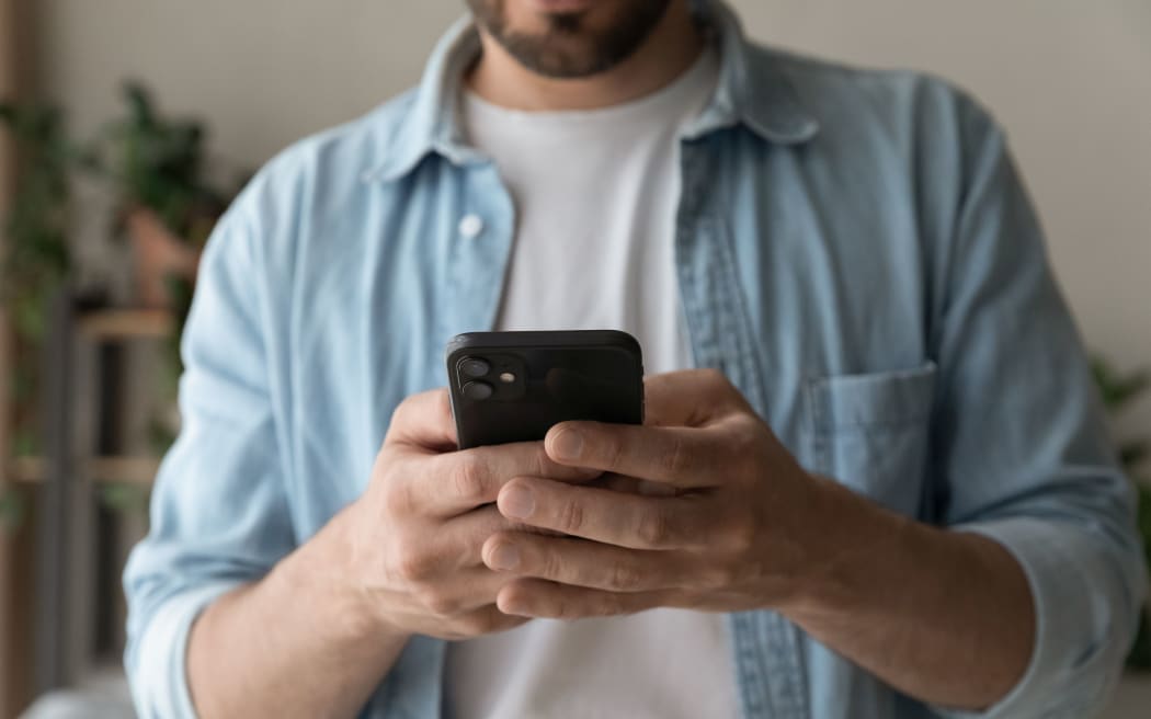 Cropped shot of young guy in casual wear using mobile phone device. Modern day millennial man