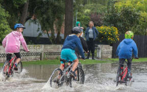 Children ride through surface flooding after the Heathcote River breached it's bank, Christchurch, New Zealand, Friday, April 14