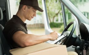 42193625 - young delivery man checking list on clipboard in van