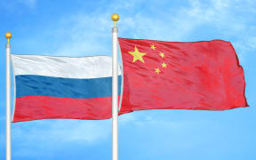 Russia and China two flags on flagpoles and blue cloudy sky background