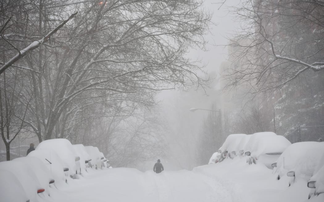 A pedestrian walks past snow-covered cars on a residential street in Washington, D.C.