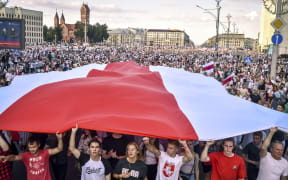 Belarus opposition supporters hold a giant former white-red-white flag of Belarus used in opposition to the government, during a demonstration in central Minsk on August 16, 2020.