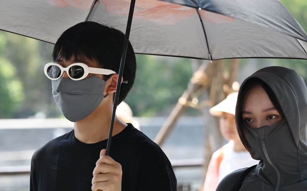 People shelter from the sun under an umbrella after visiting the Forbidden City during a heatwave in Beijing on June 24, 2023. Beijing recorded its third consecutive day of 40 degree Celsius weather, the first time since records began. (Photo by GREG BAKER / AFP)