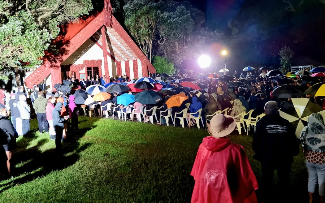 Te Whare Runanga is lit up as hundreds gather in the dark before it on the Waitangi Treaty Grounds.