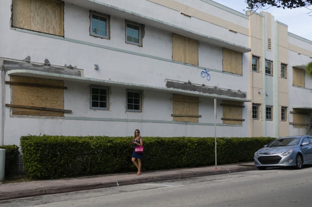 A woman walks by a building with boarded up windows during a hurricane alert for this weekend in South Miami Beach, Florida.