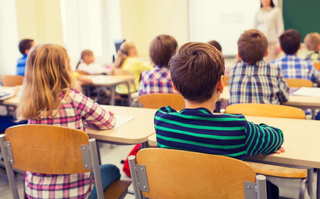 education, elementary school, learning and people concept - group of school kids sitting and listening to teacher in classroom from back