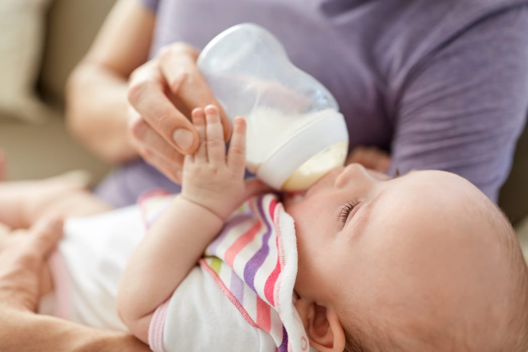 family, parenthood and people concept - close up of father feeding little daughter with baby formula from bottle at home