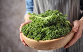 Woman holding fresh kale leaves on brown background, closeup