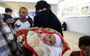 A Yemeni woman carries an ill child.