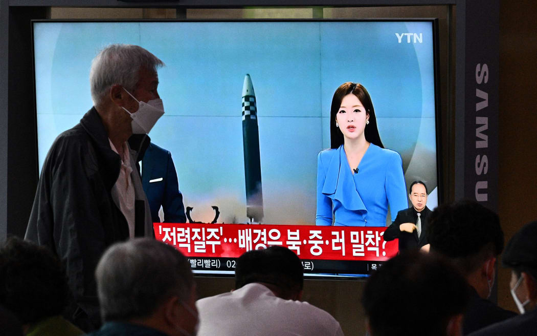Un homme passe à travers un écran montrant une émission d'information avec un fichier d'images d'un test de missile nord-coréen, dans une gare de Séoul, en Corée du Sud, le 5 juin 2022.