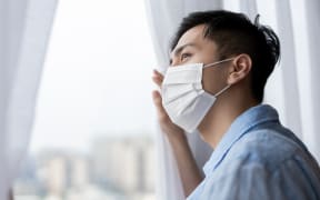 asian young man with face mask stay isolation at home for self quarantine due to an epidemic of COVID-19 and he looks out by windows. Home isolation. Isolating. Isolation. MIQ. Quaranatine