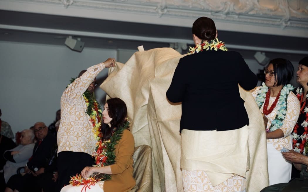 A mat is draped over Prime Minister Jacinda Ardern as part of the Samoan Ifoga ceremonial apology.