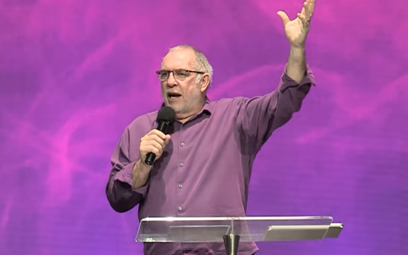 Screenshot from a Celebration Church TV Youtube video of Pastor Murray Watkinson on stage with a microphone.