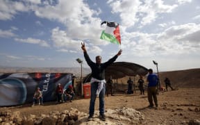 A Palestinian man raises the national flag in front of Jewish settlers during a demonstration by Palestinian and Israeli activists against the construction of Jewish settlements in the village of Ein al-Beida,