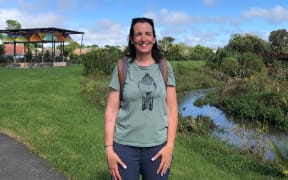 Auckland councillor Julie Fairey stands next to a stream. She is looking at the camera and smiling.