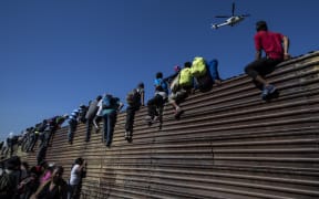 A group of Central American migrants climb a metal barrier on the Mexico-US border.