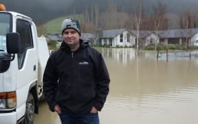 Craig Miller stands next to the flooding at a Dunedin subdivision.