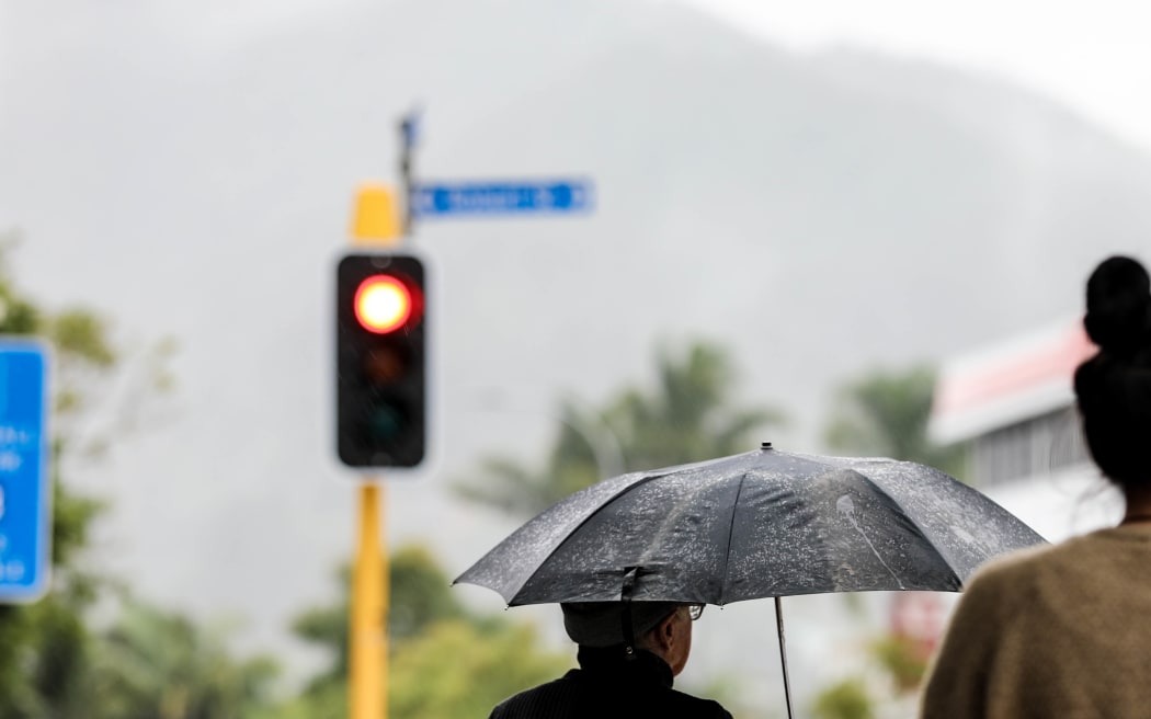 Whanarei, young and old woman stand at traffic lights, rain.