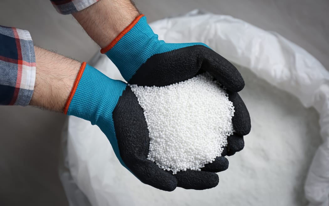 Farmer holding pile of ammonium nitrate pellets over bag, top view. Mineral fertilizer